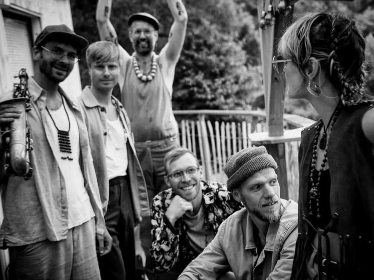 Solkatten, six band members outdoors in front of green trees, one holding a saxophone and one with his arms in the air